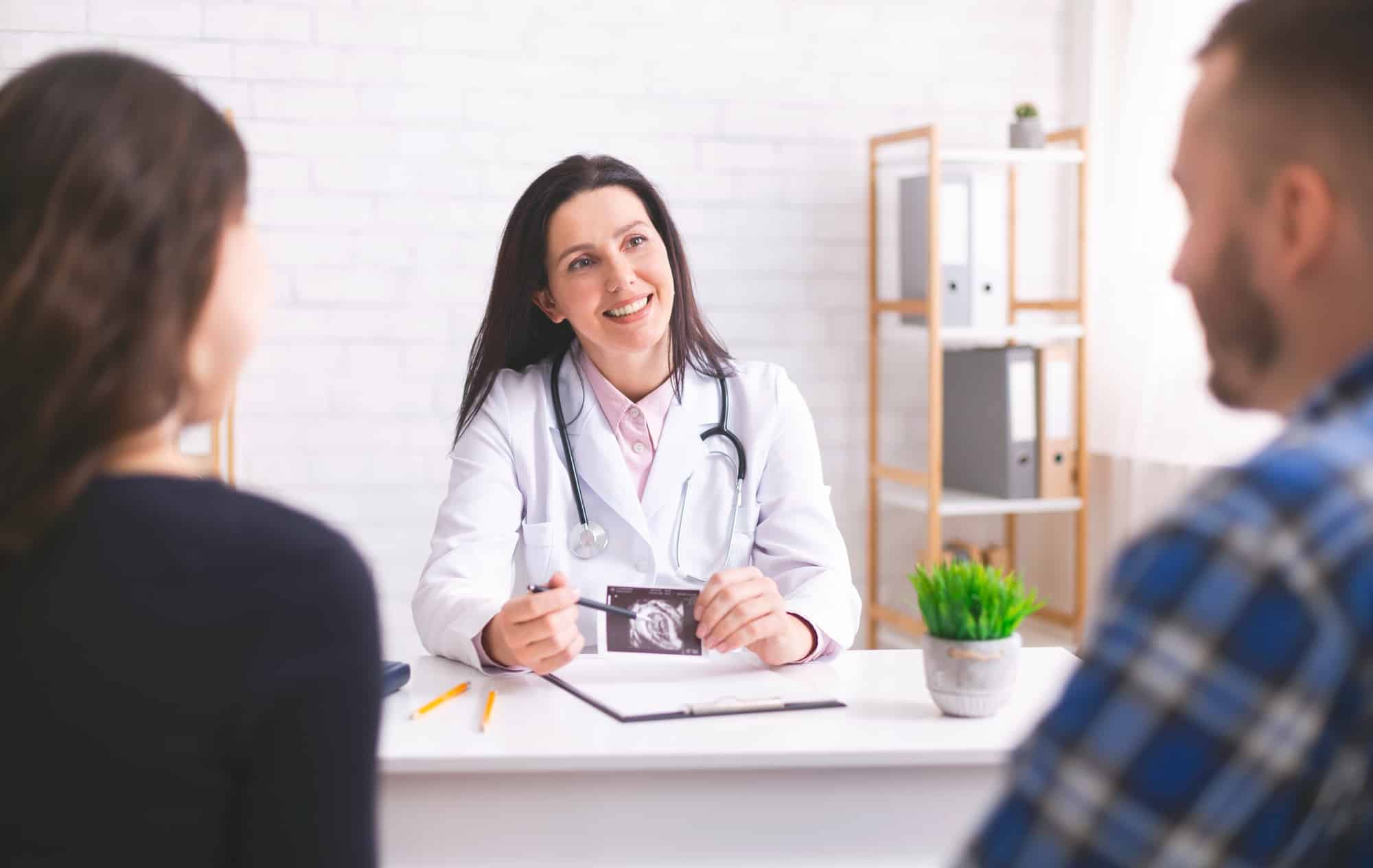 Friendly doctor explaining pregnancy diagnosis to young couple