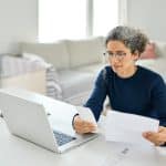Mature lady paying bills online checking medical receipts bills using laptop.