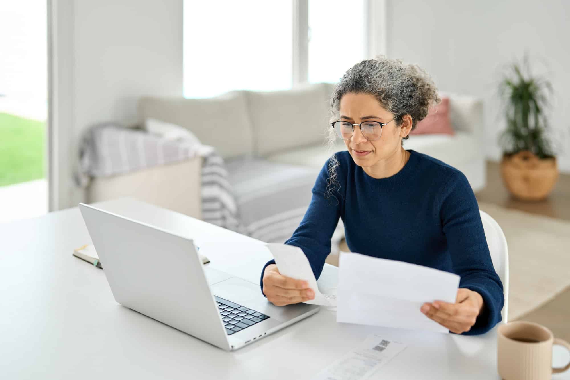 Mature lady paying bills online checking medical receipts bills using laptop.